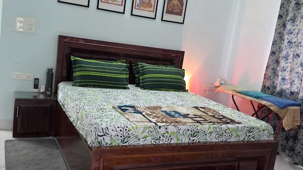 Quarto com cama de madeira, almofadas listradas em verde, mesa de cabeceira com telefone e parede decorada com quadros.