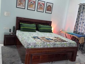 A bedroom with a wooden bed, green striped pillows, a bedside table with a phone, and a wall with framed pictures. - The Riverside Retreat is a comfortable riverfront home in the Doon Valley. India (Dehradun)