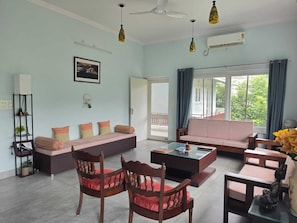 A living room with a sofa, chairs, a coffee table, and a bookshelf. - The Riverside Retreat is a comfortable riverfront home in the Doon Valley. India (Dehradun)