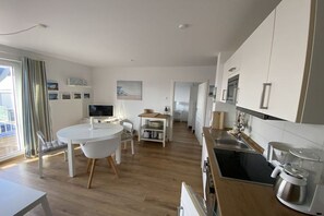 Una cuina moderna amb una illa central, una zona de menjador amb taula rodona, i vista cap a l'exterior a través d'una porta corredissa.