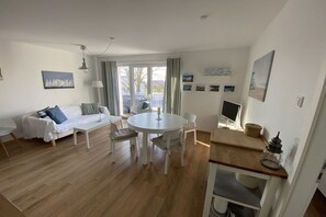 A modern living room with a sofa, a dining table with chairs, a TV, and a lamp. - Baltic Sea Oasis Rerik (Ostseebad Rerik)