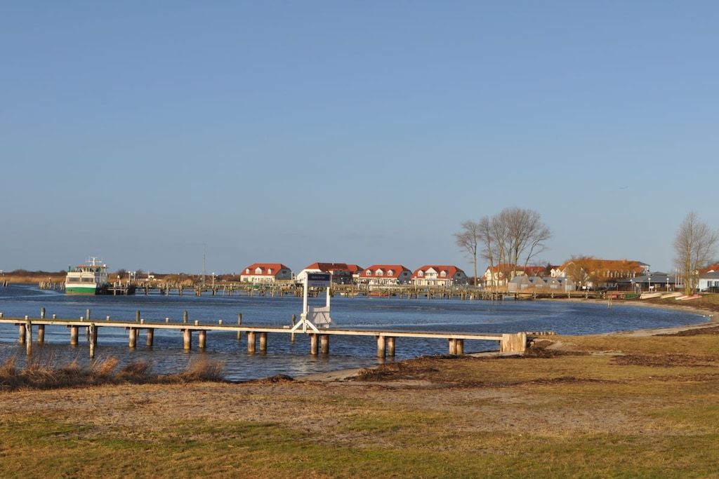 Een pand aan het water met een steiger die in het water uitloopt, omringd door huizen met rode daken.
