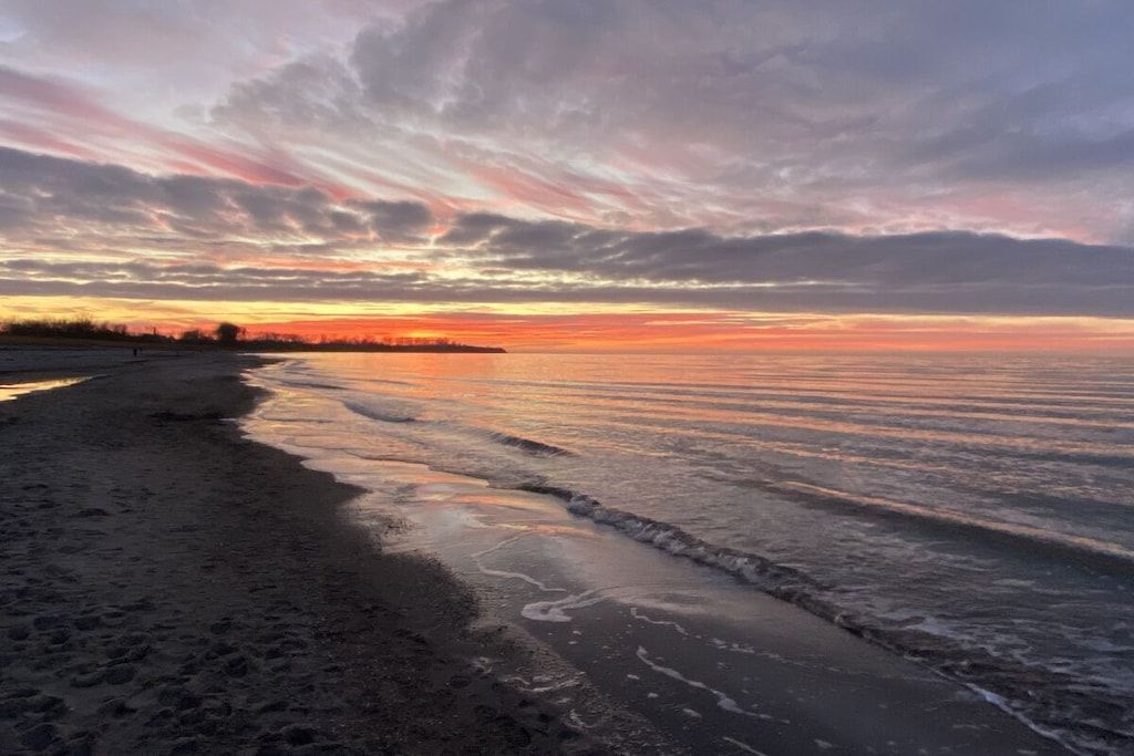 A beach with a sunset, waves, and a distant shoreline.