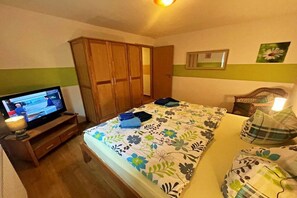 Un dormitorio con cama, televisor sobre un mueble de madera, armario y espejo en la pared.