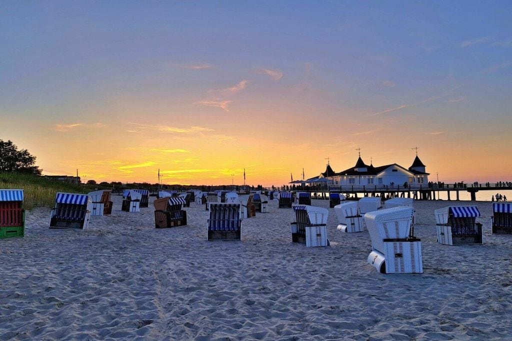 Ein Strand mit Reihen von Liegestühlen und einem Steg, im Hintergrund ein Gebäude.