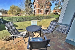 Un patio al aire libre con una mesa redonda y cuatro sillas, un seto y un edificio al fondo.