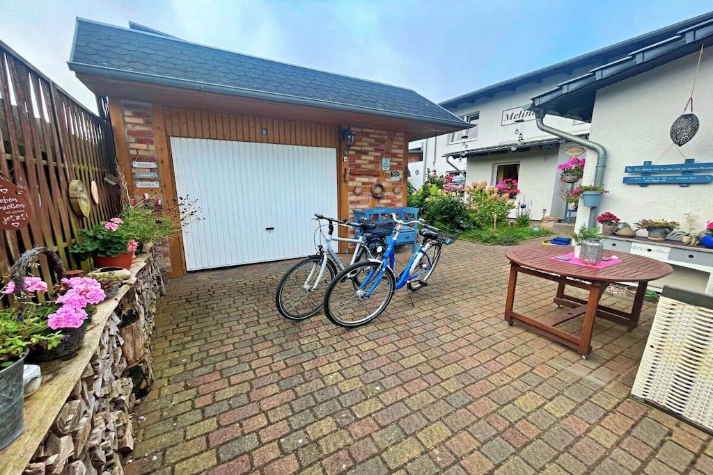 Un cortile con pavimento in mattoni, due biciclette, un tavolo di legno e un portone garage bianco.