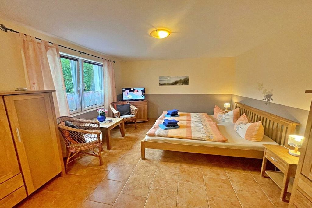 A bedroom with a bed, a desk, a television, and a window.