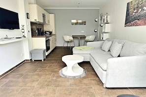 A modern living room with a grey sofa, a white coffee table, and a kitchen area in the background. - Holiday apartment Altenberg 02 (Ahlbeck (Seebad))
