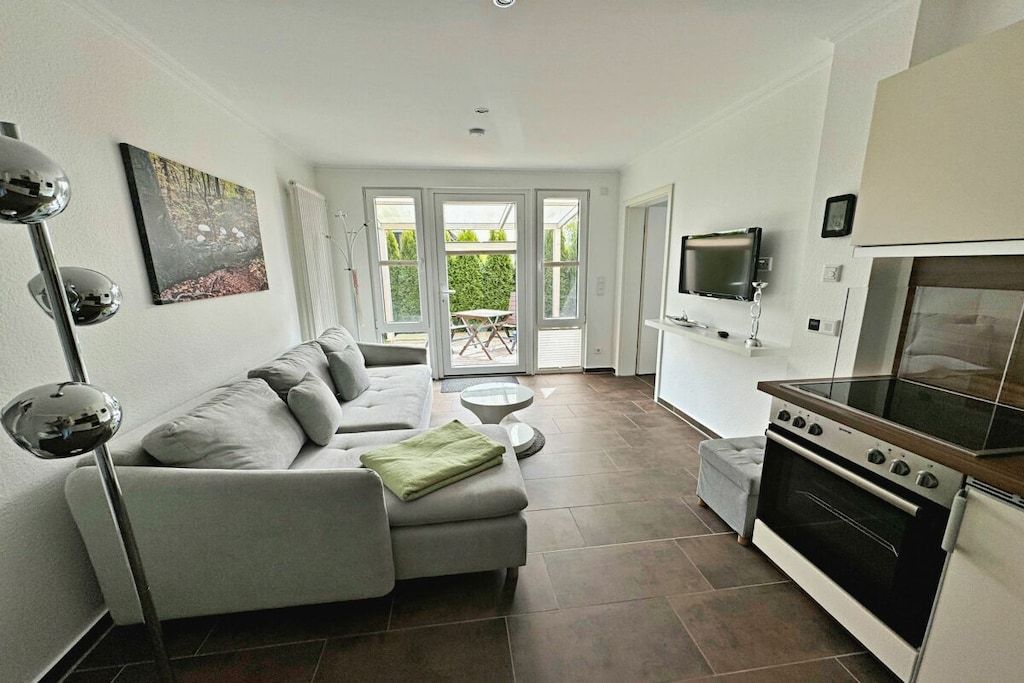 A modern living room with a sofa, a television, and a kitchen area with an oven.