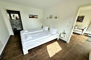 A bedroom with a large bed, a bedside table, a nightstand, a built-in shelf, and a door leading to a bathroom. - Holiday apartment Altenberg 02 (Ahlbeck (Seebad))