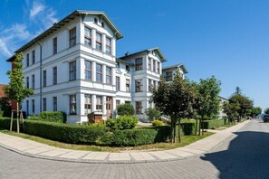 Ein mehrgeschossiges Wohngebäude mit einer symmetrischen Fassade, einem zentralen Eingang und einem gepflegten Garten.
