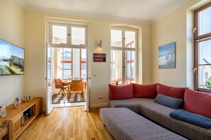Ein gemütlicher Wohnbereich mit einer Couch, einem Esstisch mit Stühlen und einem Fernseher auf einer Holzkommode.
