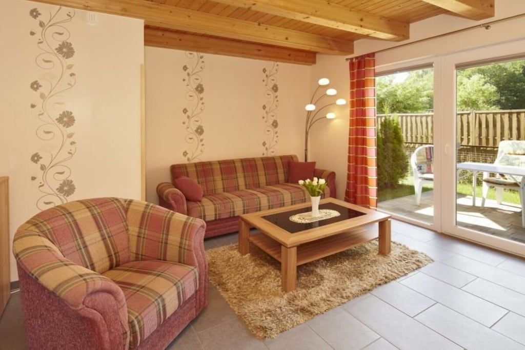 A living room with a plaid sofa, a matching armchair, a coffee table, and a large window with curtains.