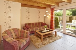 Ein Wohnzimmer mit einem karierten Sofa, einem passenden Sessel, einem Couchtisch und einem großen Fenster mit Vorhängen.