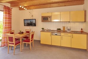Eine Küche mit gelben Schränken, einer Mikrowelle und einem Spülbecken. Ein Esstisch mit Stühlen und ein Bild an der Wand sind ebenfalls vorhanden.