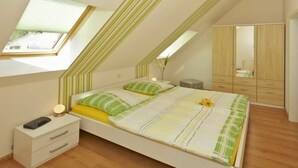 Una camera da letto con soffitto spiovente, un letto con biancheria a righe, un comodino con una lampada e un armadio.