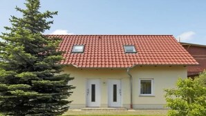 Una casa a due piani con tetto in tegole rosse, due porte bianche e una piccola finestra al piano superiore.