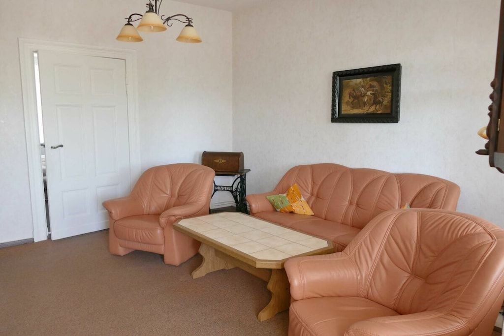 Ein Zimmer mit beigeem Teppich, einer weißen Tür, einem beigen Sofa, einem kleinen Tisch und einer Nähmaschine.