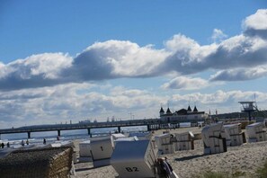 En strand med strandhytter, en pir och en byggnad med flera tornspiror.