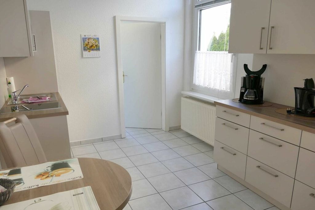 Eine Küche mit Fenster, weißen Schränken, einer Kaffeemaschine und einem gefliesten Boden.