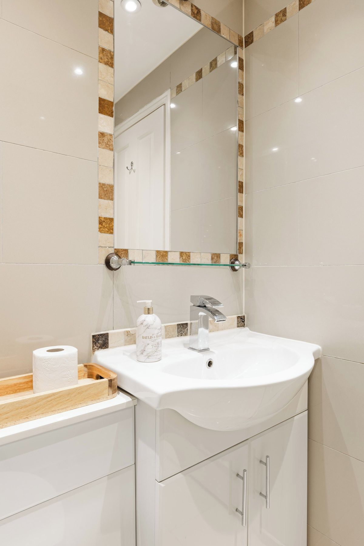 Casa de banho moderna com lavatório branco, prateleira de vidro e espelho com moldura decorativa.