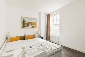 A hotel room with a bed, a painting, a window with curtains, and a nightstand with a lamp. - New! Spacious 1BR Flat | Marble Arch | Hyde Park (Greater London)