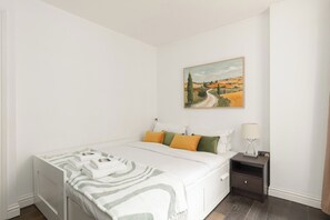 A bedroom with a bed, pillows, a nightstand, a lamp, and a painting on the wall. - New! Spacious 1BR Flat | Marble Arch | Hyde Park (Greater London)