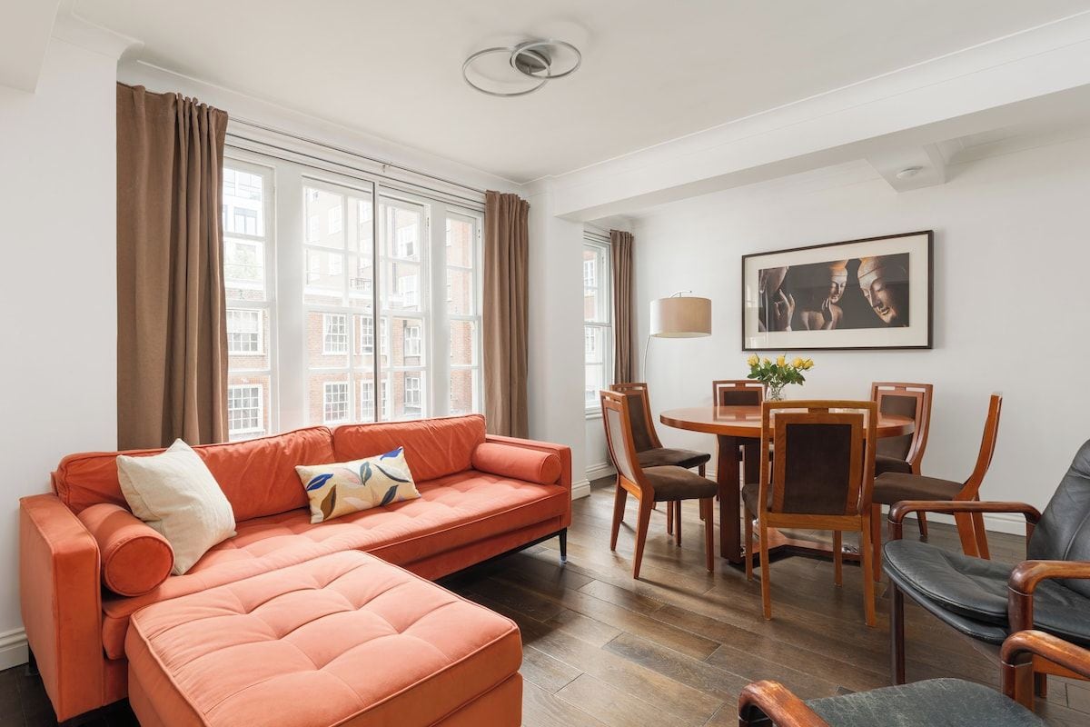 Una sala de estar con un sofá, una mesa de comedor con sillas y una ventana con cortinas.