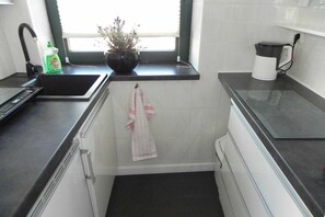 Eine Küche mit schwarzem Arbeitsplatz, einer Spüle, einem Wasserkocher und einem Blumentopf am Fensterbrett.