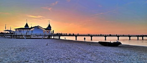 A beach with a pier extending into the water, a boat docked on the shore, and a building with a cross on top.