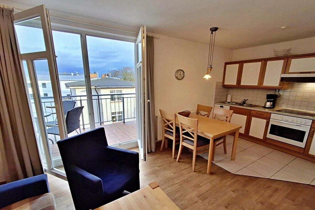 Une cuisine moderne avec des meubles en bois, un coin repas comprenant une table et des chaises, et une grande porte-fenêtre coulissante donnant sur un balcon.