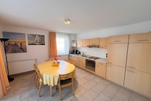 A compact kitchen with a dining table, wooden cabinets, and a window with curtains. - Ground floor 05 Holiday apartment at Wilhelmsberg (Ahlbeck (Seebad))