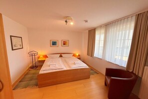 Ein Hotelzimmer mit Bett, Sessel, Stehlampe und einem Fenster mit Vorhängen.