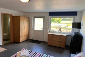 Quarto com guarda-roupa de madeira, escrivaninha com gavetas, janela com vista e chuveiro.