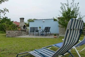 A patio area with a stone chimney, a table with chairs, and a striped lounge chair. - Feldmann holiday accommodations (Korswandt)