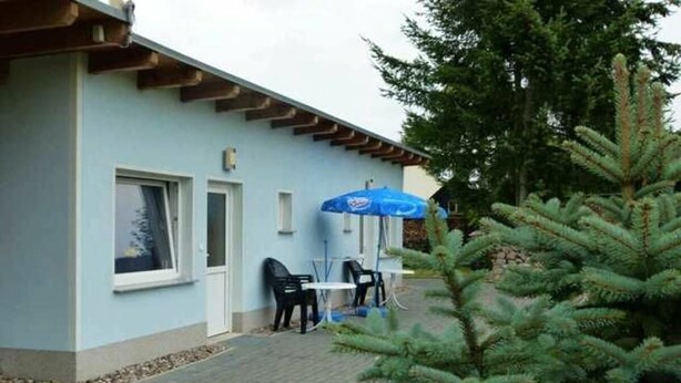 Un edificio blu chiaro con un portico, posti a sedere all'aperto e un pino.