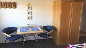Una stanza con un'armadio in legno, un tavolino con tovaglia a quadri, due sedie blu e una parete con quadri appesi.