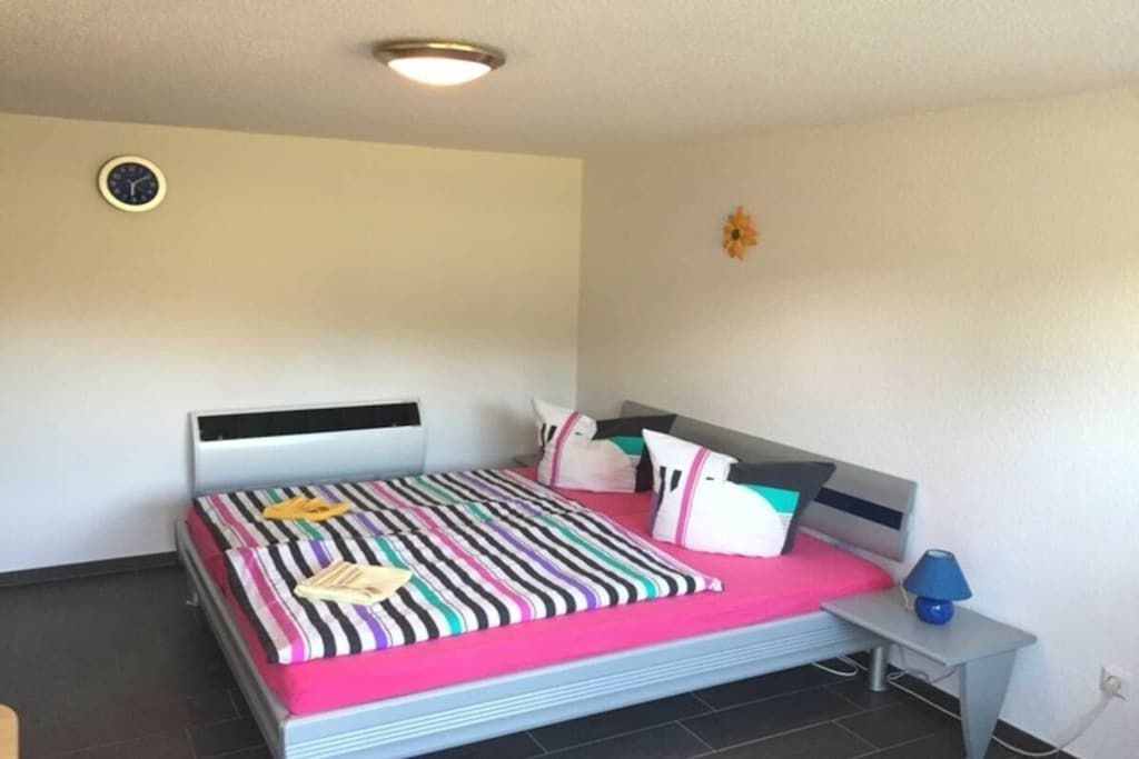 Ein Schlafzimmer mit einem Bett, einem Nachttisch mit Lampe, einer Wanduhr und einer kleinen Dekoration.