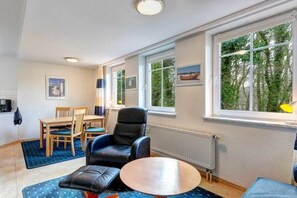 Ein Zimmer mit Esstisch, Stühlen, einer Couch, einem Couchtisch und großen Fenstern mit Blick auf Bäume.