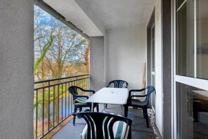 Ein Balkon mit Tisch und Stühlen, einem Geländer und Blick auf Bäume und Gebäude.