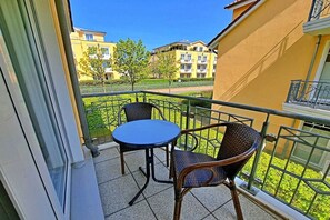 Un balcon avec une table et deux chaises, donnant sur un quartier résidentiel avec des immeubles et de la verdure.