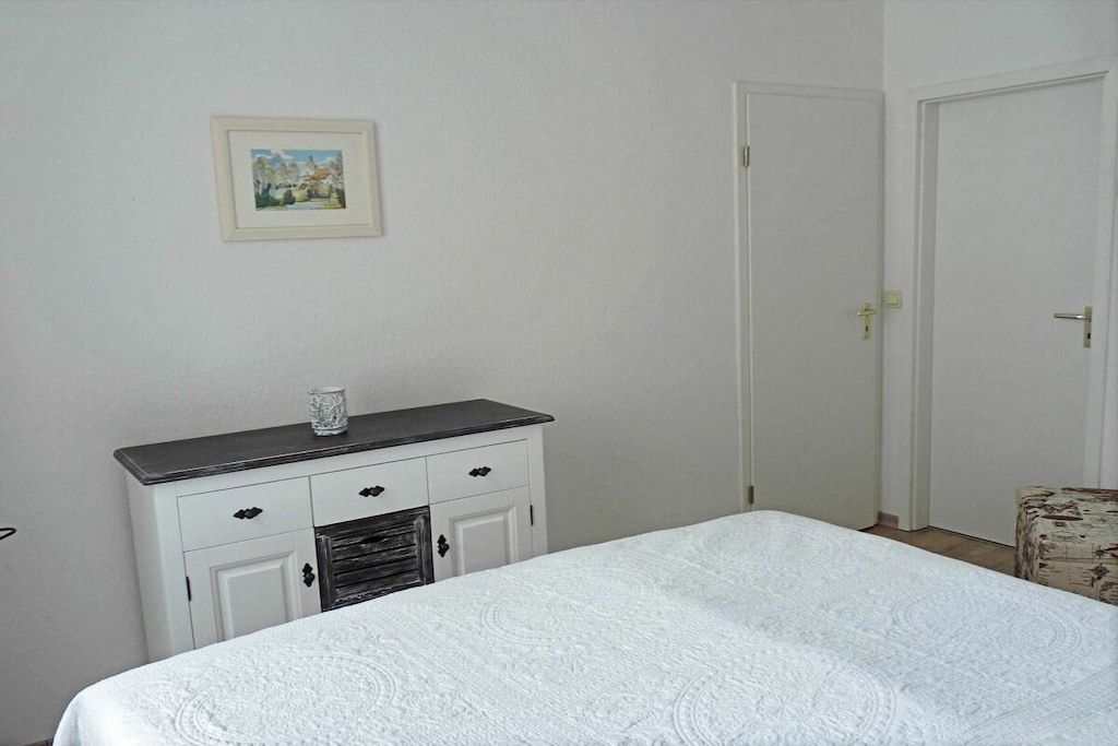 A bedroom with a bed, a dresser, a door, and a framed picture on the wall.