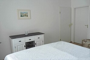 Une chambre à coucher avec un lit, une commode, une porte et un tableau encadré au mur.