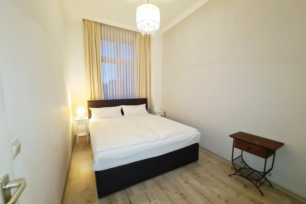 Ein Schlafzimmer mit einem Bett, einem Nachttisch, einer Lampe und einem kleinen Holznachtkästchen.