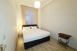 Ein Schlafzimmer mit einem Bett, einem Nachttisch, einer Lampe und einem kleinen Holznachtkästchen.