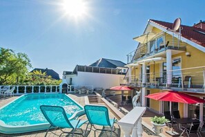 Ein Schwimmbecken mit Liegestühlen, ein Essbereich mit Sonnenschirmen und ein Gebäude mit einem Balkon.