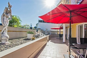 Une terrasse extérieure agrémentée d’une statue, d’un parasol rouge et d’un espace salon.