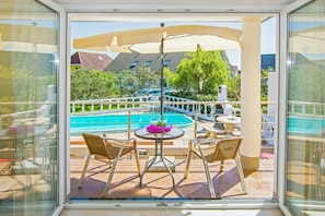 Ein Balkon mit Blick auf einen Swimmingpool, Gartenmöbel und einem großen Sonnenschirm.