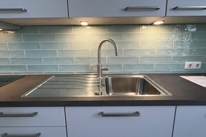 A kitchen with a stainless steel sink, a modern faucet, and a tiled backsplash. - Villa Franz Josef 04 (Heringsdorf (Seebad))